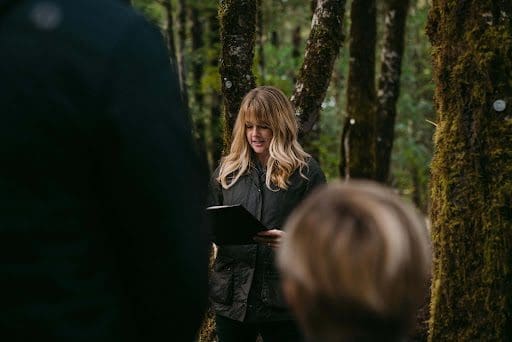 Woman speaking at a memorial service in a forest. She has scripture readings for funerals