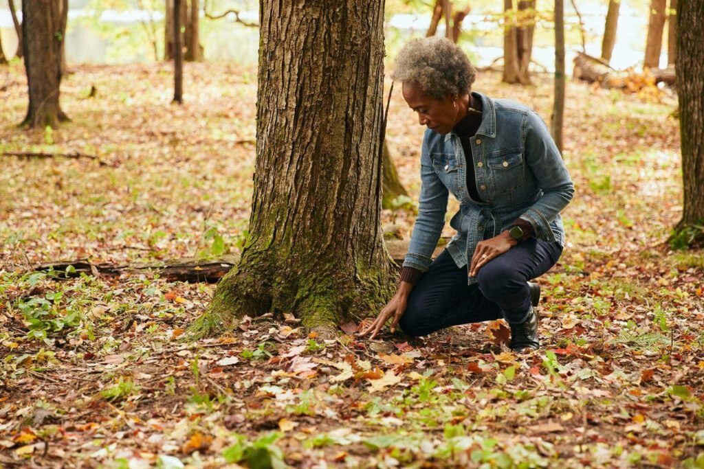 A woman kneels at the memorial tree of her spouse at Better Place Forests St. Croix Valley. She has thought about what to say when scattering ashes