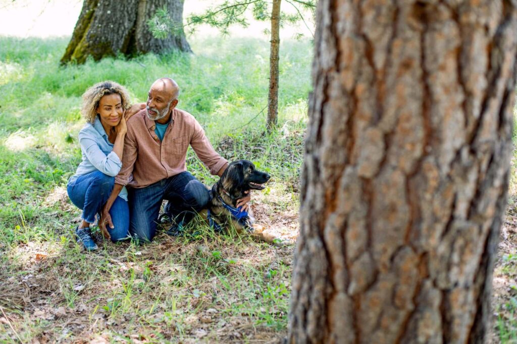 A man and woman kneel at the base of memorial tree with their pet dog beside them.