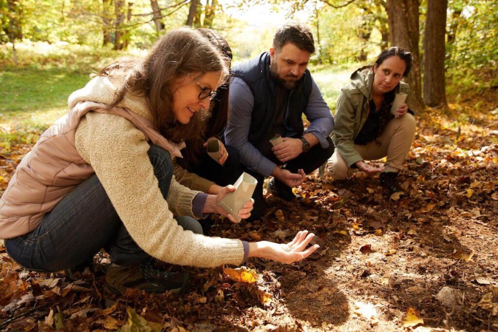 Siblings at a forest ceremony spreading wildflower seeds under a tree to honor their parent
