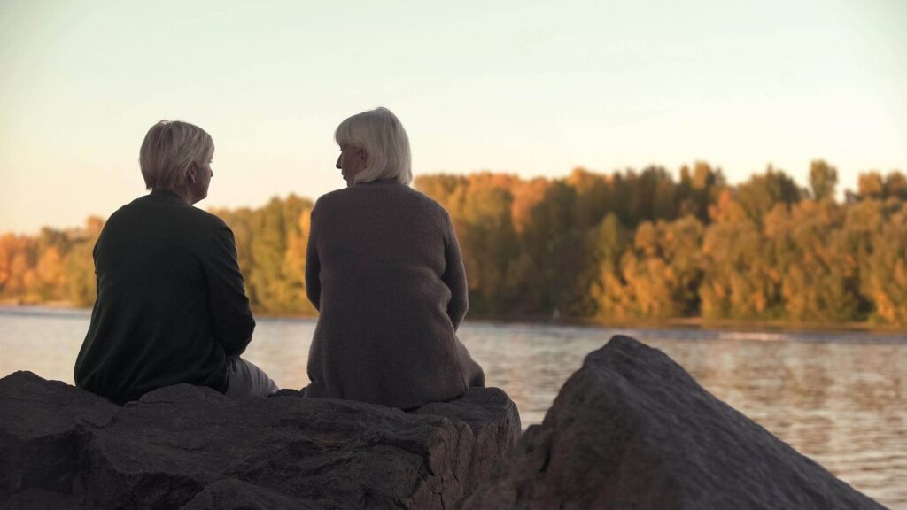 Two women sitting by a lake talking about how to support family on hospice care