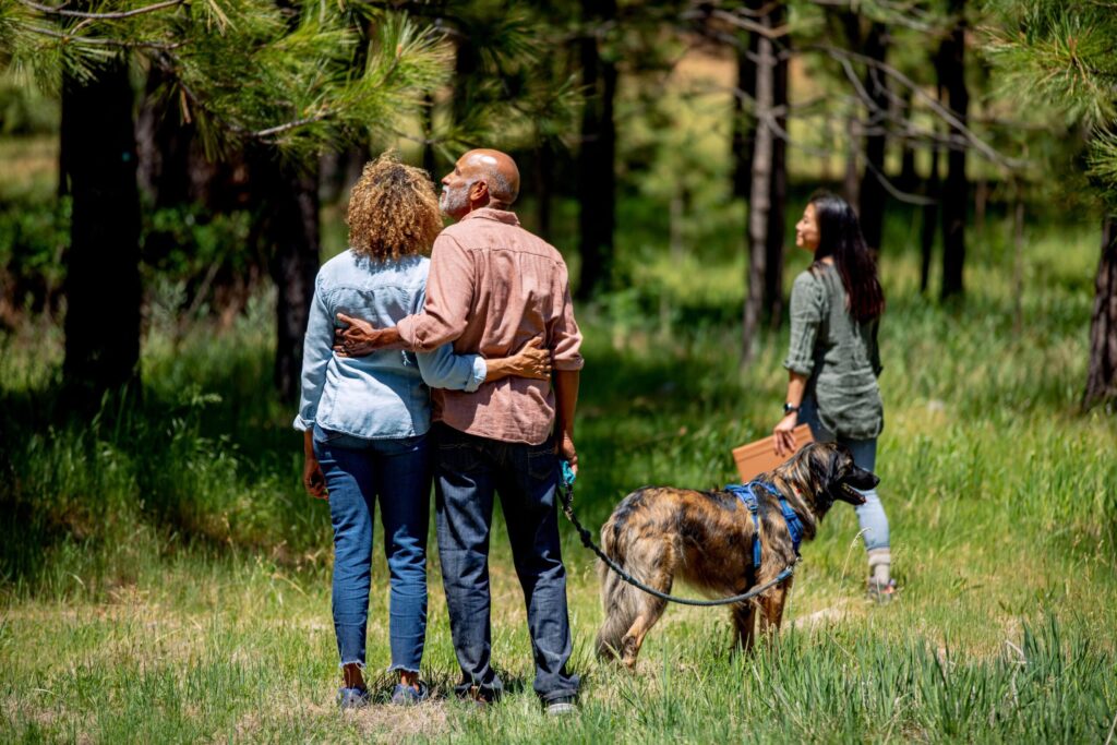 a couple admires Better Place Forests meadow with a forest guide and their dog