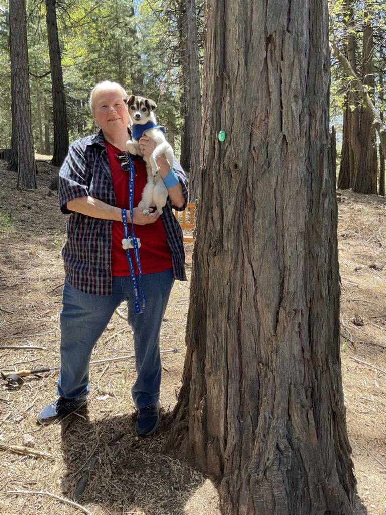 woman holding her dog in front of her memorial tree