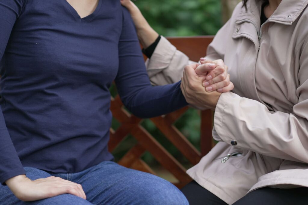 Closeup of woman reaching for grieving friend’s hand
