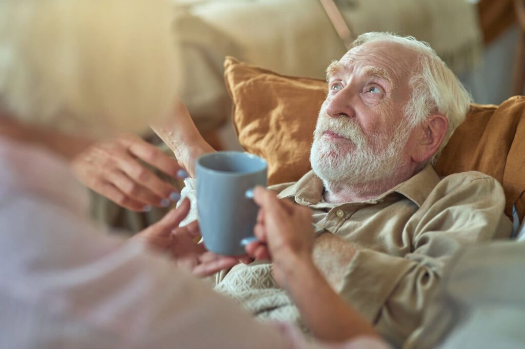 handing elderly hospice care patient a warm cup of tea