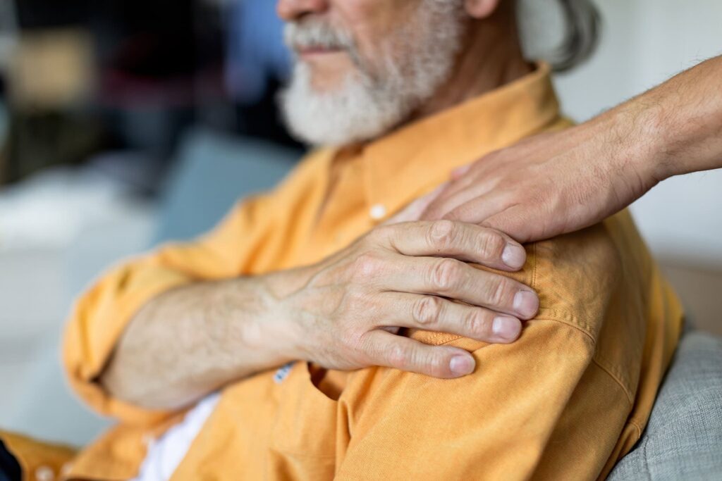 Close up of son and his senior father at home hand placed on shoulder in support and comfort.