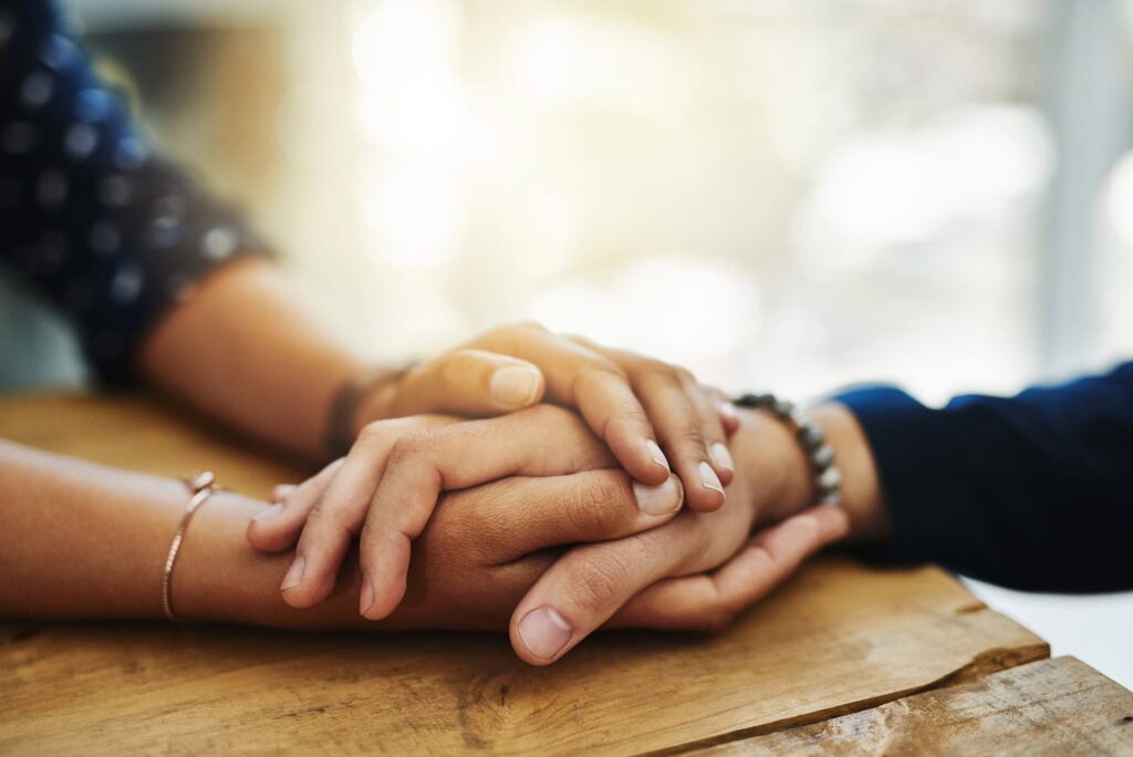 Closeup of friends holding hands, showing care and love through a hard time, consoling each other and bonding