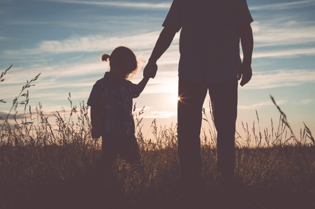 Silhouette view of a father holding his daughter’s hands
