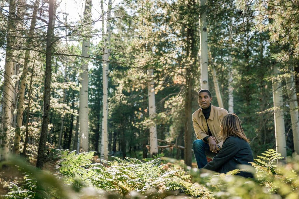 a couple sits in a lush forest of aspen trees in Flagstaff Memorial Forest