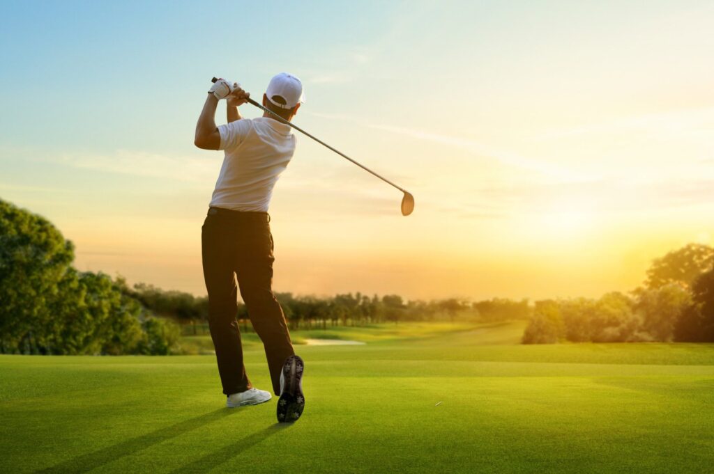 Golfer hit sweeping driver after hitting golf ball down the fairway with sunset background.