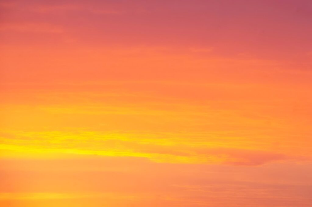 A gradient sunset sky in shades of deep orange, golden yellow, and soft pink.