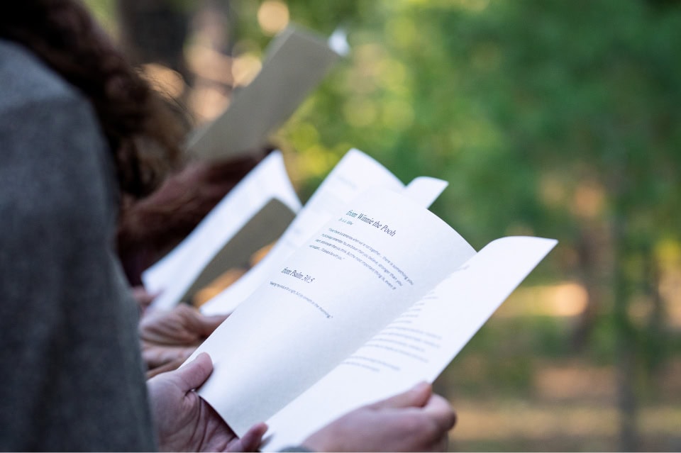 Close-up of hands holding a booklet outdoors, with a blurred forest background.